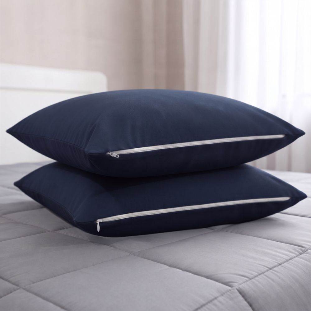 Two navy blue pillowcases stacked on a gray quilted bedspread in a softly lit bedroom setting.
