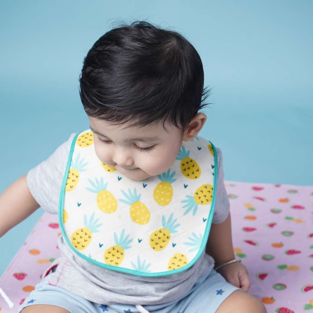 Baby-wearing-printed-bib-and-sitting-on-playmat