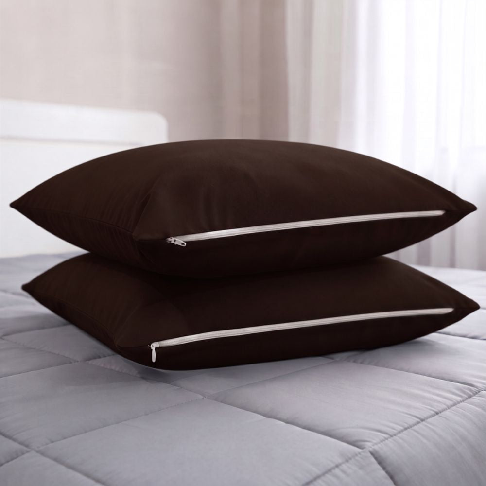 Two dark brown pillowcases stacked on a light gray quilted bedspread in a softly lit bedroom setting.