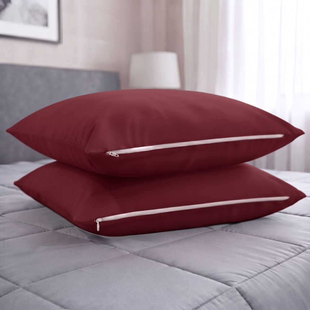 Two burgundy pillowcases stacked on a grey quilted bedspread in a softly lit bedroom setting.