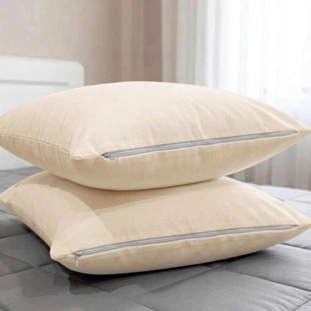 Two beige pillowcases stacked on a gray quilted bed, with a softly blurred bedroom background.
