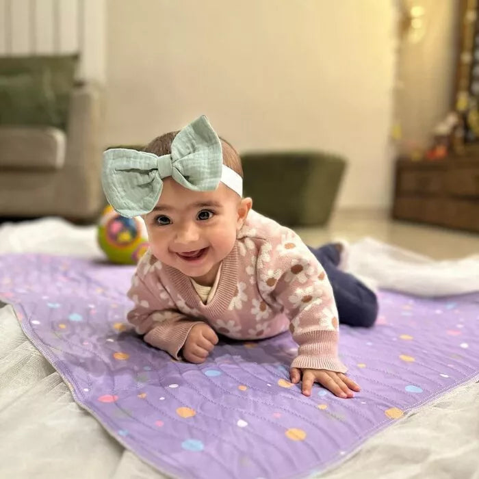 Baby lying on a Happy Matty polka dots print bed protector mat